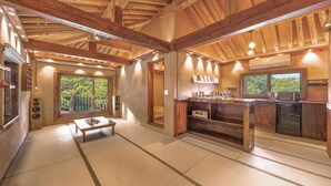Una habitación tradicional japonesa con suelo de tatami, techo de madera y vistas a la vegetación.