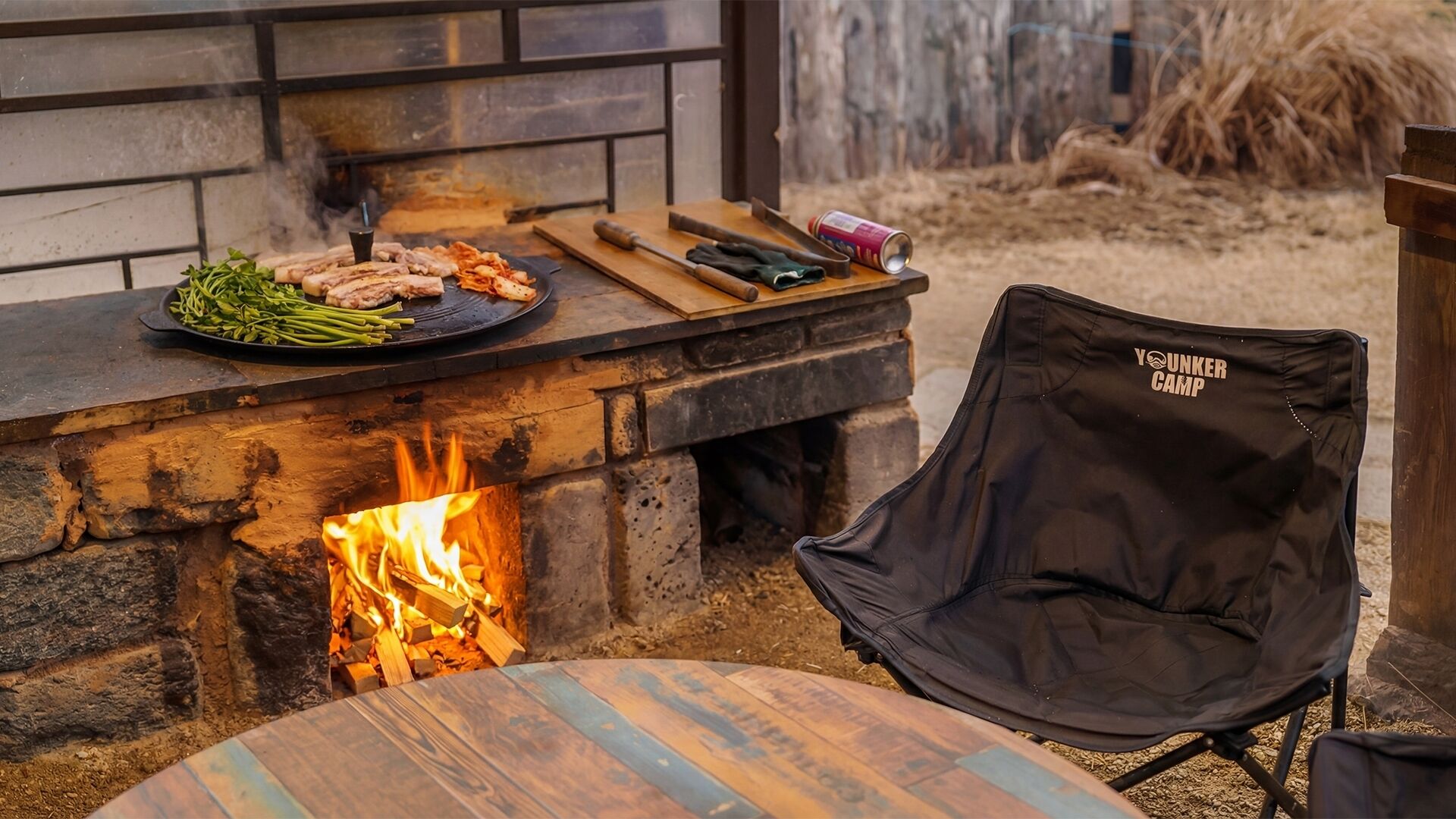 Ein Steinkamin mit Grill, ein Stuhl und ein Tisch mit einem Holzscheit.