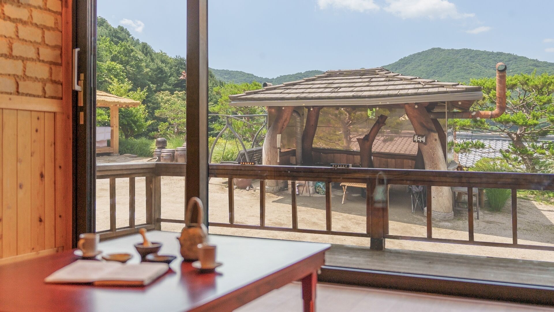 Ein Zimmer mit Holztisch, Blick auf eine traditionelle Struktur und eine Berglandschaft.