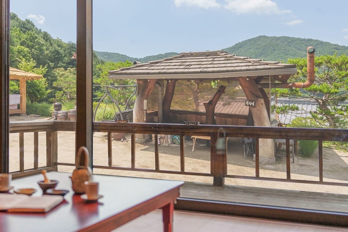 A room with a wooden table, a view of a traditional structure, and a mountainous landscape.
