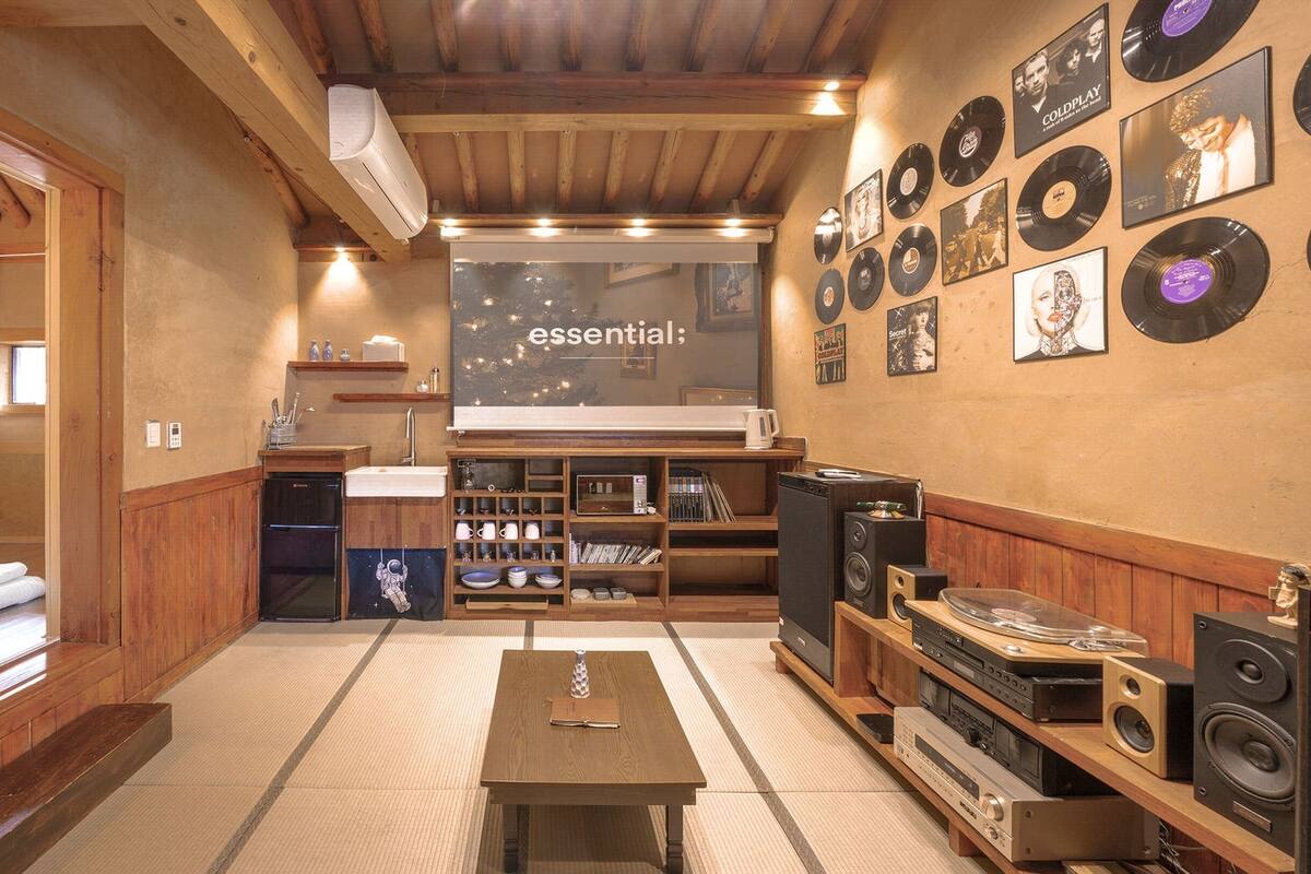A cozy room with a wooden floor, a bed, a TV, a shelf with records, and a speaker system.