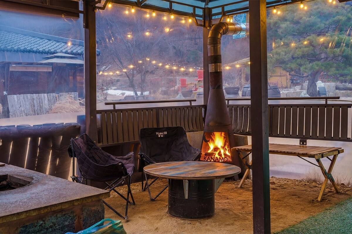 An outdoor seating area with a wood-burning stove, chairs, a table, and a view of a traditional building.