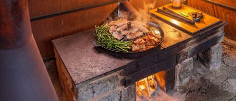 Un barbecue coréen traditionnel, avec un gril, des légumes et de la viande servis sur une table en pierre, une lanterne et une bouteille de sauce à proximité.