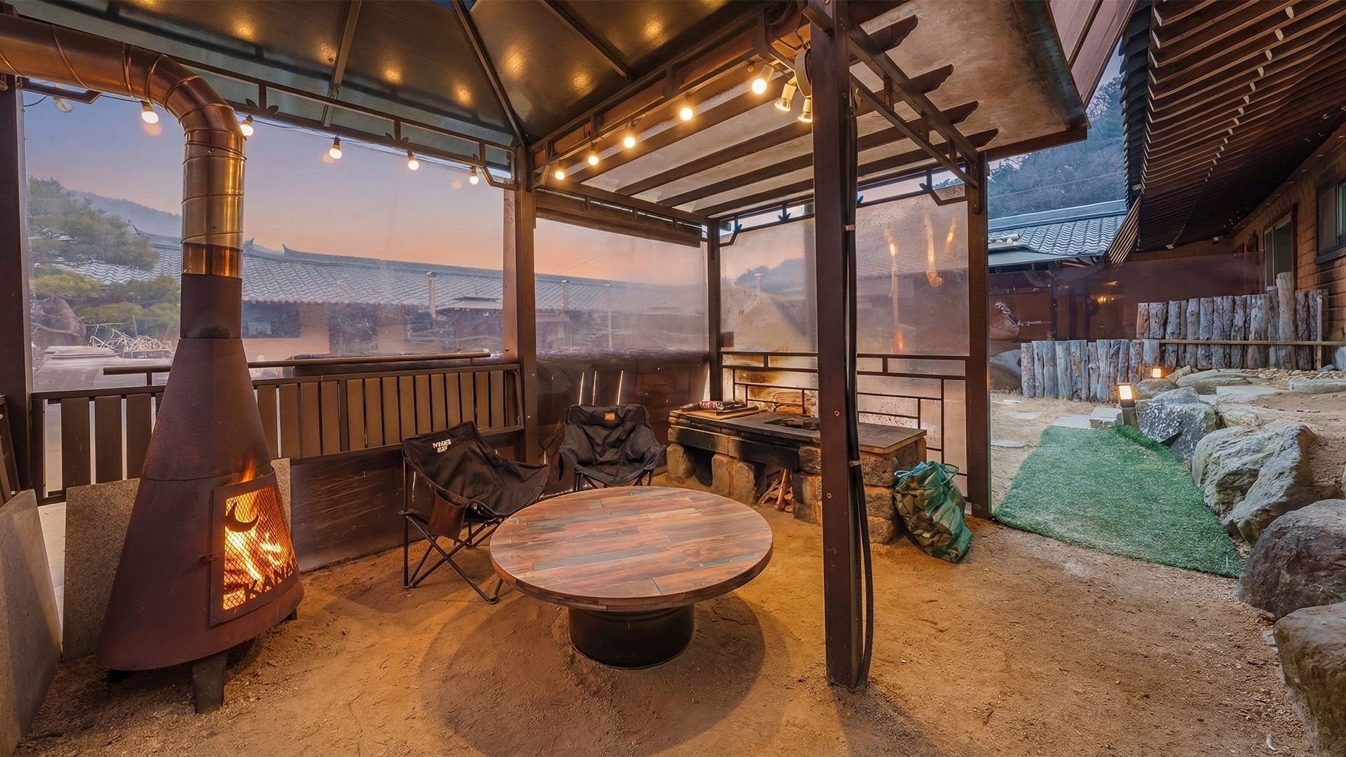 Ein Sitzbereich im Freien mit einem runden Tisch, einem Grill und Blick auf die Landschaft.
