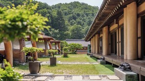 Un edificio japonés tradicional con un corredor cubierto, plantas en macetas y montañas al fondo.