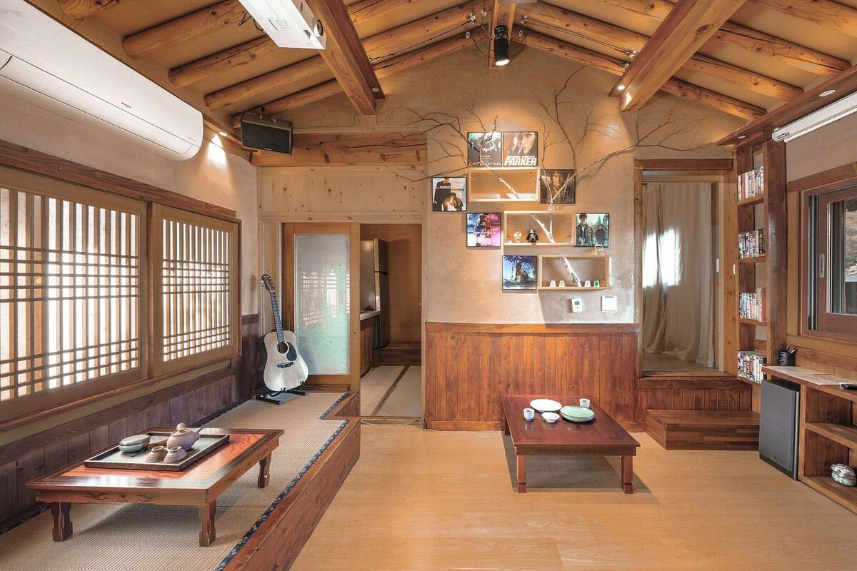 A traditional Japanese-style room with tatami flooring, a low wooden table, a guitar, and a bookshelf with movie posters.