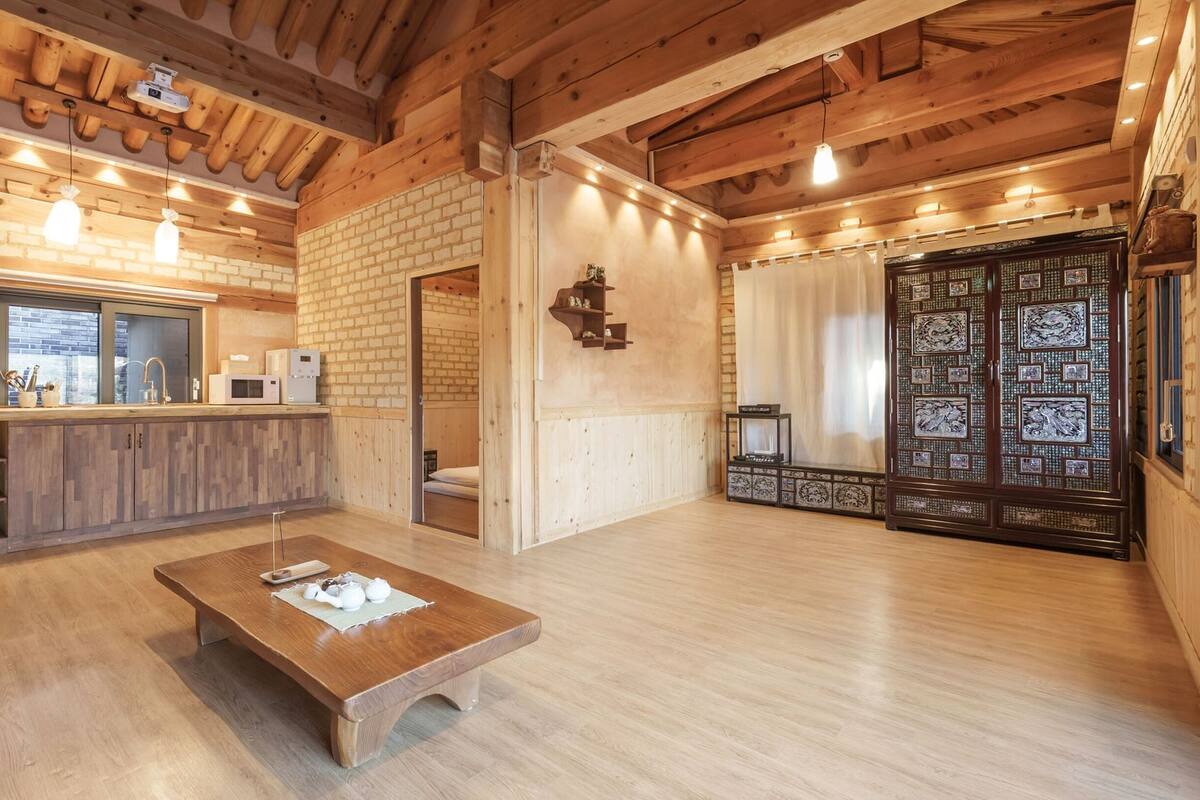 A spacious kitchen with wooden beams, a brick wall, and a large wooden table.
