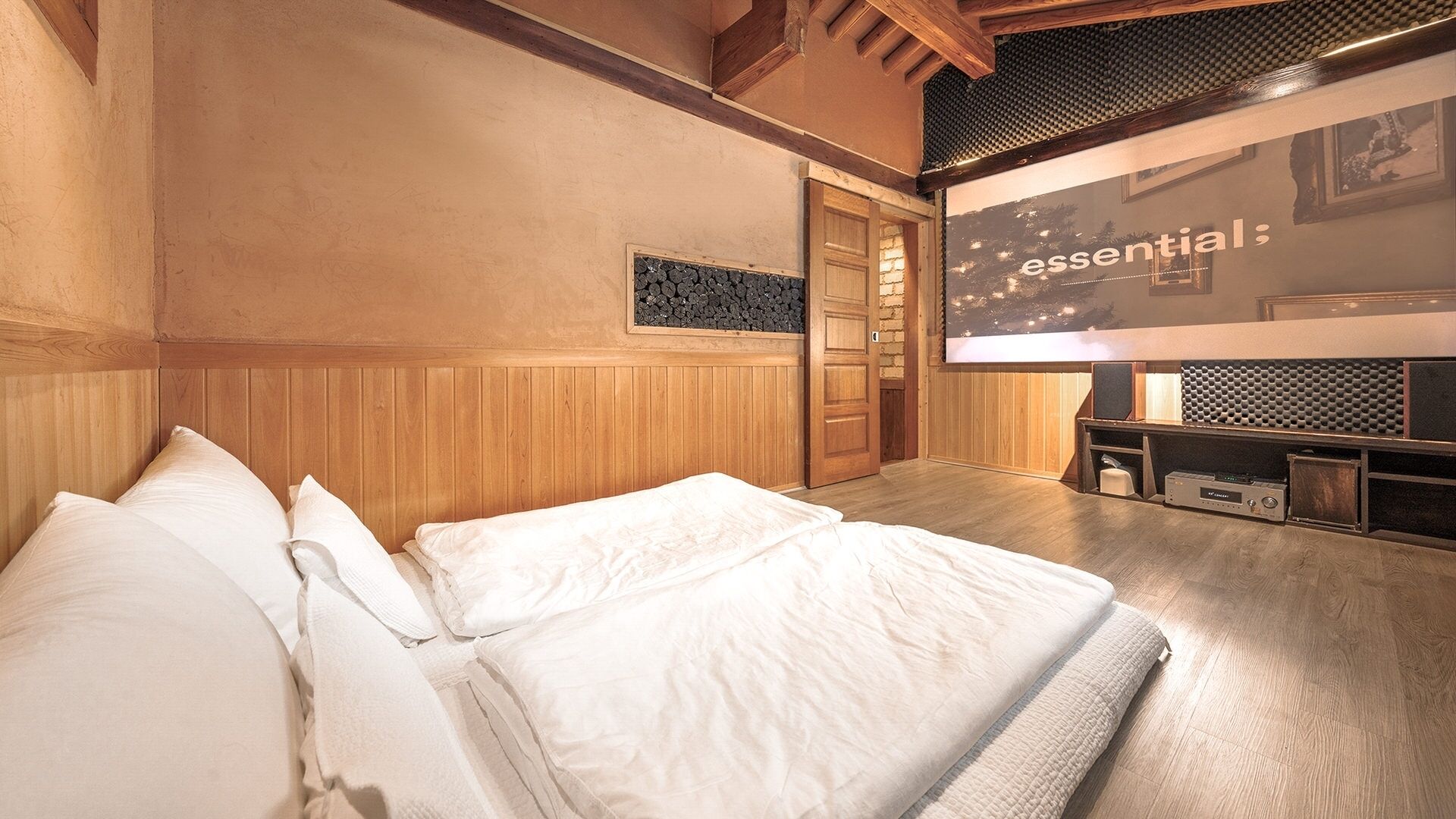 Ein Schlafzimmer mit einem Bett, einer Holzverkleidung, einer Tür und einem an der Wand montierten Bildschirm, der 'essential' anzeigt.