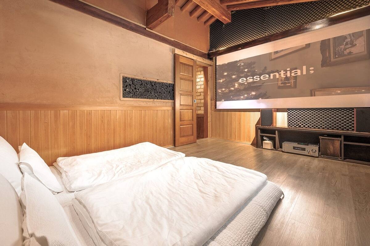 A bedroom with a bed, a wooden wall panel, a door, and a wall-mounted screen displaying 'essential:'.