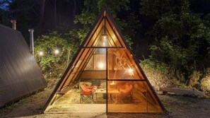 Une structure triangulaire en verre abritant une table et des chaises, entourée d’arbres.