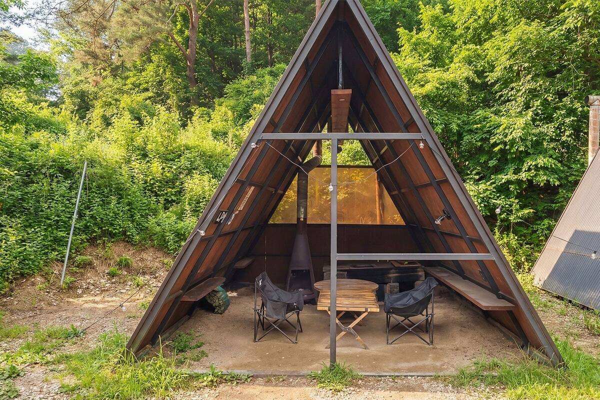 A triangular metal structure with a table and chairs inside, surrounded by greenery.