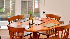 A round wooden table with four chairs, a bottle of wine, and two glasses on a placemat. - Bright & Perfectly Located! - Pass the Keys (Cardiff)