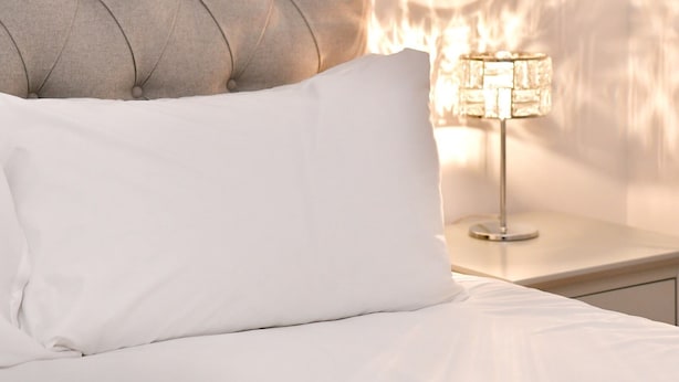 A neatly made bed with a tufted headboard and a white pillow, a bedside table with a lamp, and a wall switch. - Bright & Perfectly Located! - Pass the Keys (Cardiff)