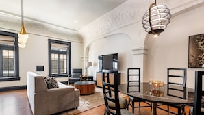 A spacious living room with a sofa, a dining table with chairs, a TV, and a chandelier.