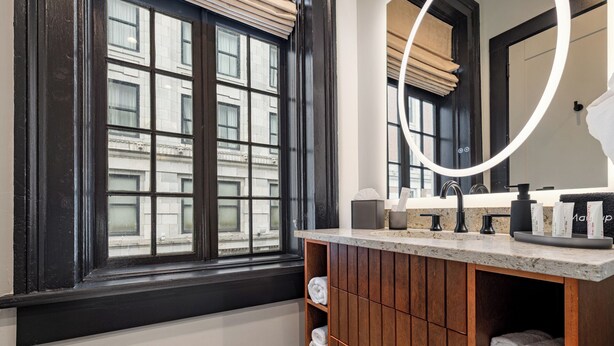 A bathroom with a large window, wooden vanity, and a mirror with a circular light.