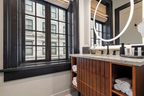 Een badkamer met een groot raam, een houten wastafelmeubel en een spiegel met rondom verlichting.