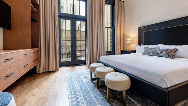 Ein modernes Hotelzimmer mit einem großen Bett, einer Holzkommode, einem Fernseher und Blick durch eine Glastür nach draußen.