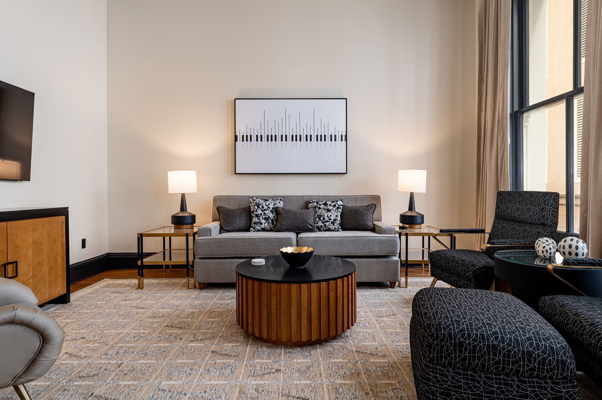 Ein modernes Wohnzimmer mit einem grauen Sofa, zwei Nachttischen mit Lampen, einem runden Couchtisch und gemusterten Sesseln.