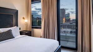 Una habitación de hotel moderna con una cama grande, una mesita de noche, una lámpara de pared y un ventanal con cortinas.