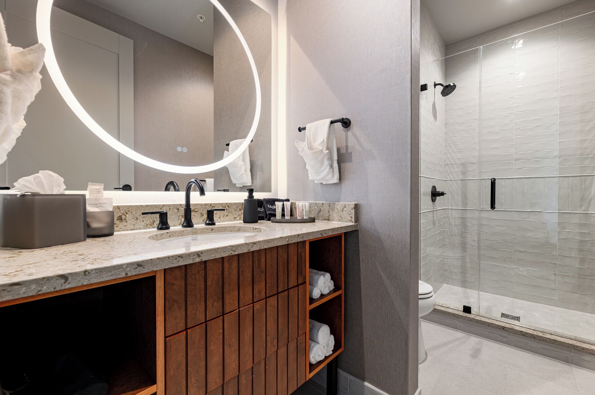 A modern bathroom with a vanity, a large mirror, a shower enclosure, and a towel rack.
