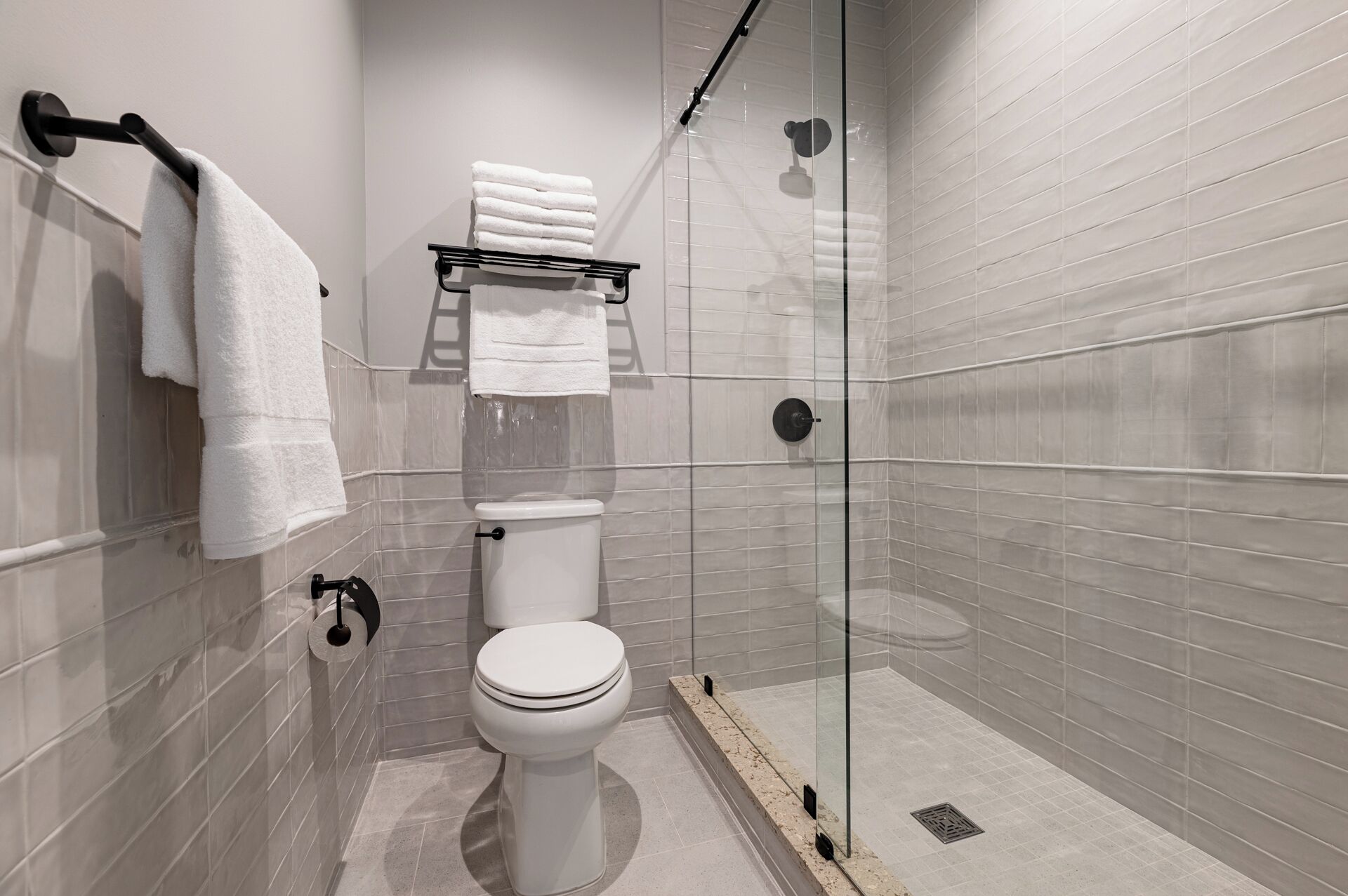 A modern bathroom with a glass shower enclosure, a toilet, and a towel rack with folded towels.