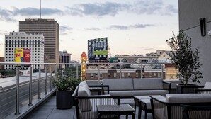 A rooftop terrace with outdoor seating, a large billboard, and city buildings in the background. - 4BR Exclusive Downtown Group Penthouse | The Mayfair (New Orleans)