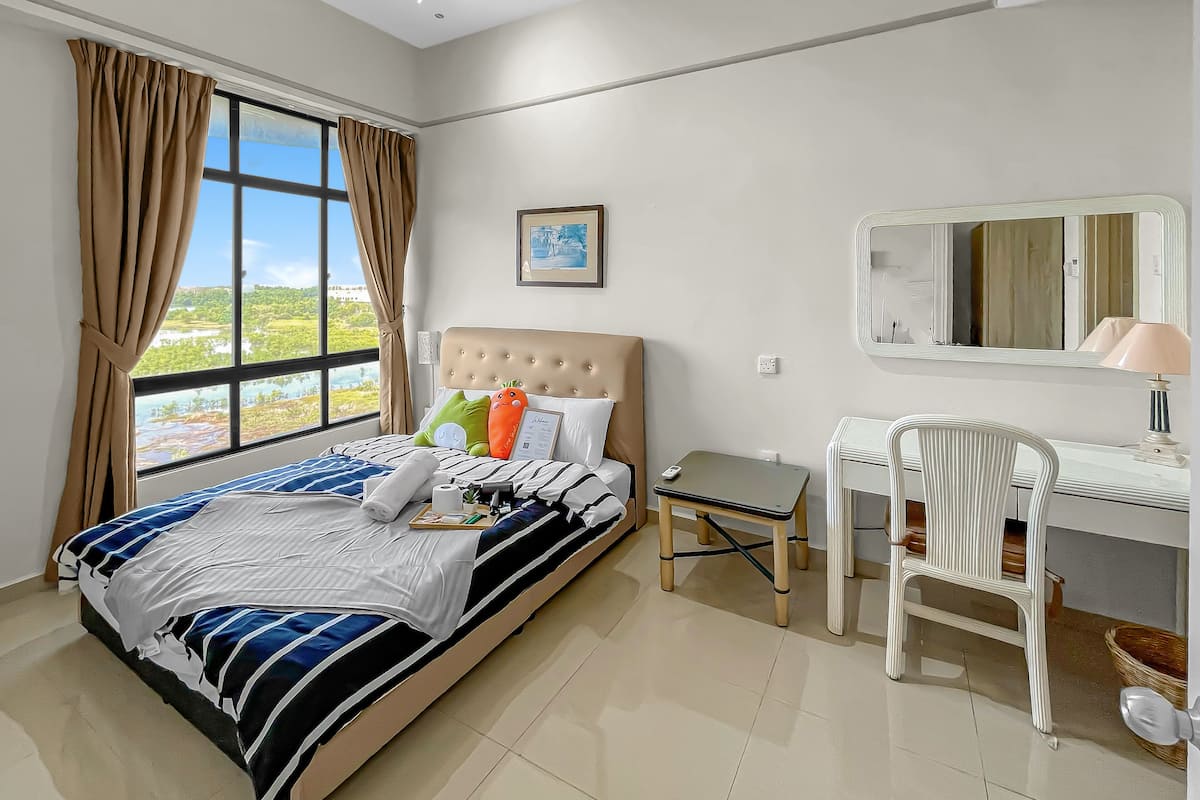 A bedroom with a bed, a bedside table, a chair, a mirror, and a window with curtains.