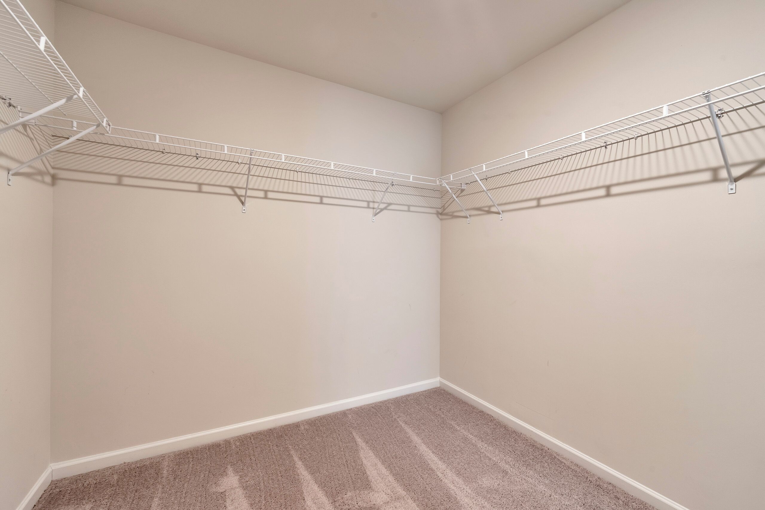 Une chambre d’angle aux murs et au tapis de couleur beige, équipée d’une étagère en fil de métal.