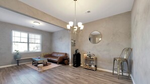 A spacious living room with a brown leather sofa, a coffee table, and a chandelier. - Electric & Vibrant home 15 min from Downtown ATL (Decatur)
