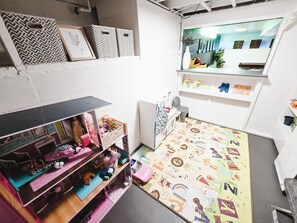 Ein gemütlicher Raum mit einer Puppenhaus-Dekoration, einem gemusterten Teppich und einem Fenster mit Blick auf Gebäude.