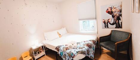 A bedroom with a bed, a chair, a small table, and a window.