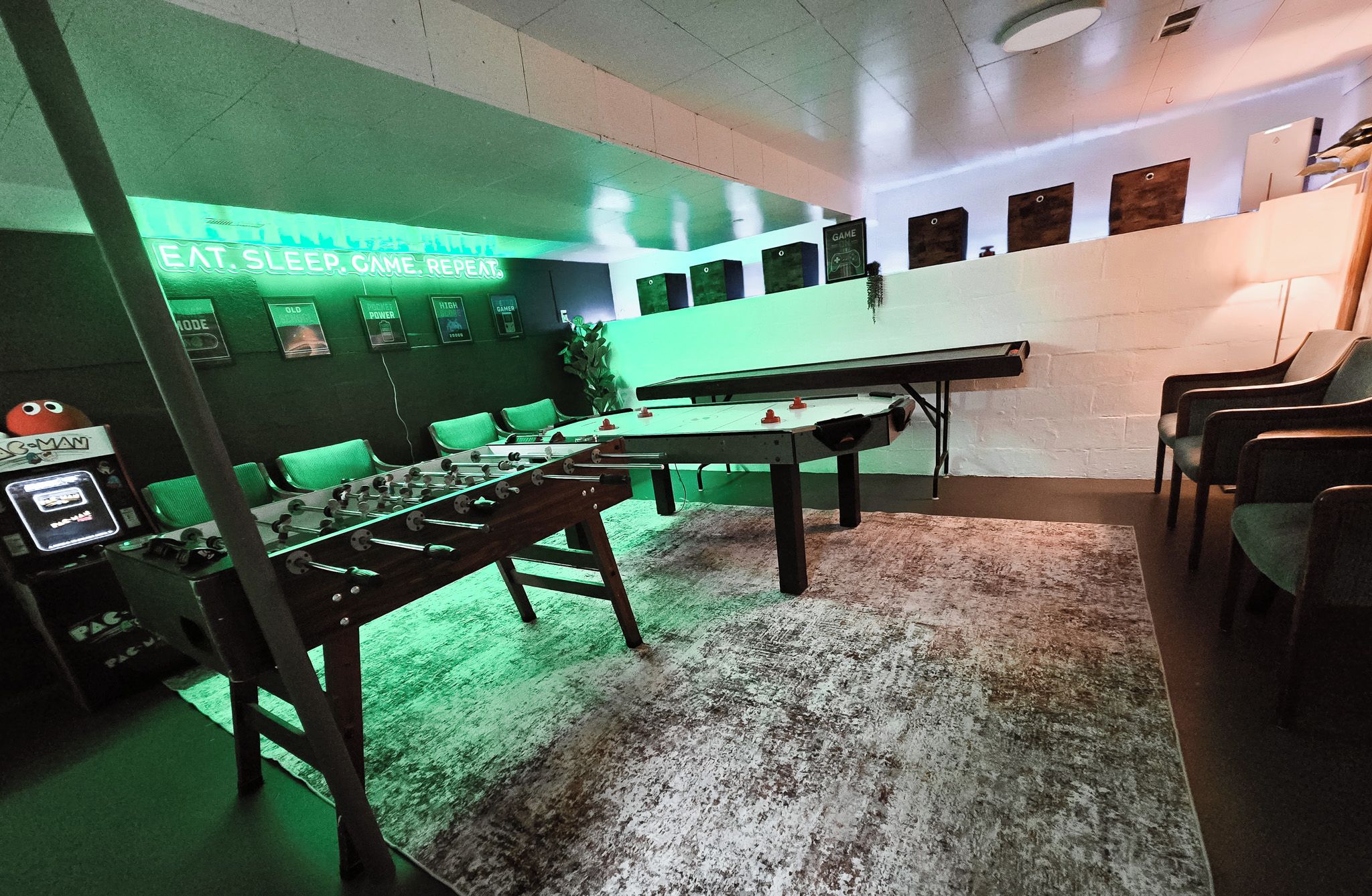 A room with a foosball table, green chairs, and a wall with game-related posters.