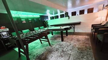 A room with a foosball table, green chairs, and a wall with game-related posters.