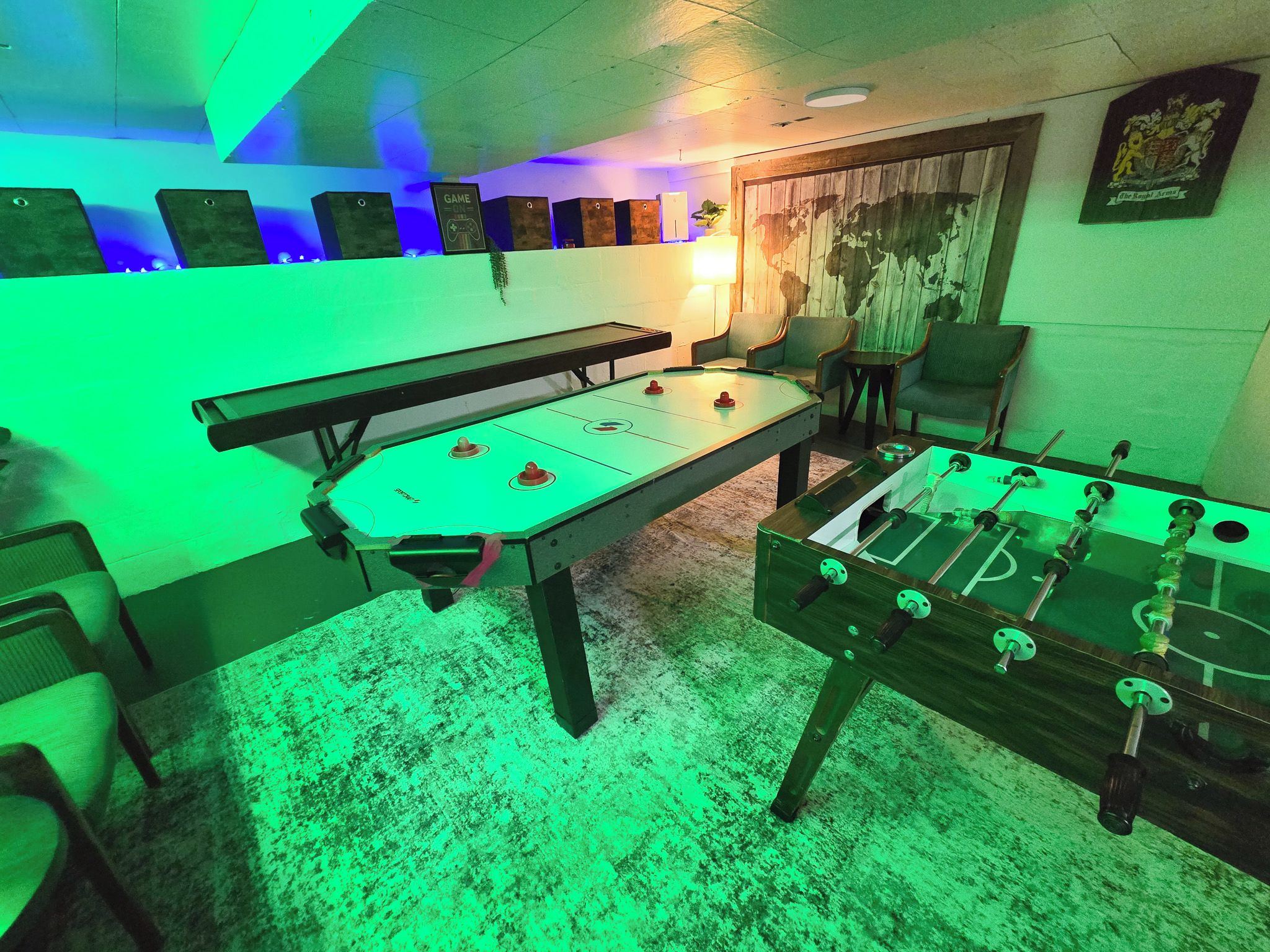Een kamer met een tafelvoetbaltafel en een pooltafel, beide met groene verlichting.