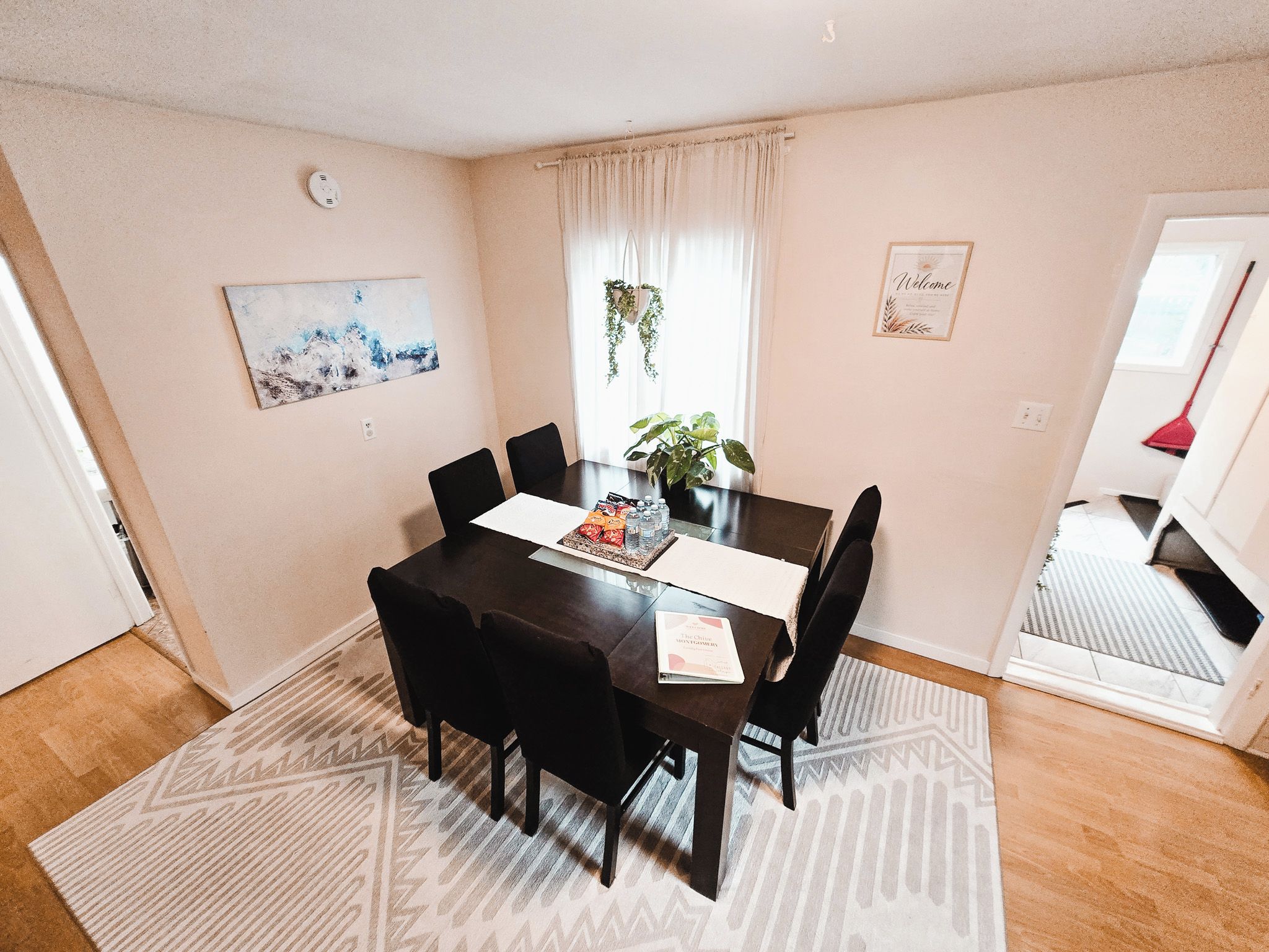 Een eetgedeelte met een tafel, stoelen, een plant en een schilderij aan de muur.