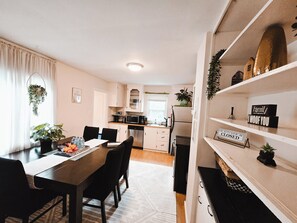 A modern kitchen with white cabinets, a dining area with a wooden table and chairs, and a kitchen sign indicating it is closed. - The Fern | Hot Tub • Arcade • Games • Playground (Calgary)