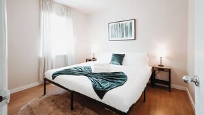 A bedroom with a bed, two bedside tables, a nightstand, a framed picture on the wall, and a door. - Stay & Play - Central Family Friendly (Calgary)