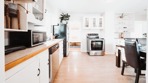 A modern kitchen with white cabinetry, a microwave, stove, and a dining area with a table and chairs. - Stay & Play - Central Family Friendly (Calgary)