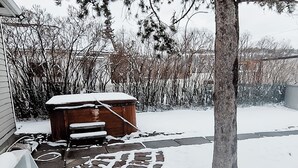 A snow-covered backyard with a hot tub, a tree, and a stone pathway. - Stay & Play - Central Family Friendly (Calgary)