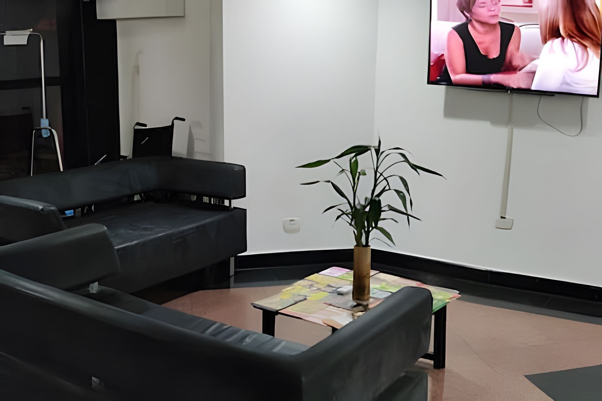 A modern waiting area with black leather sofas, a small table with a plant, and a TV mounted on the wall.