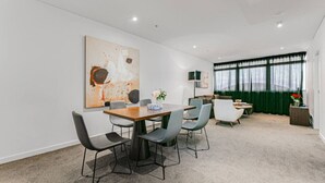 A modern dining area with a wooden table and grey chairs, a large abstract painting on the wall, and a green curtain in the background.
