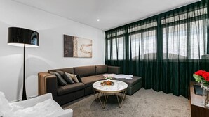 A modern living room with a sectional sofa, a round coffee table, a floor lamp, and a large window with sheer curtains.