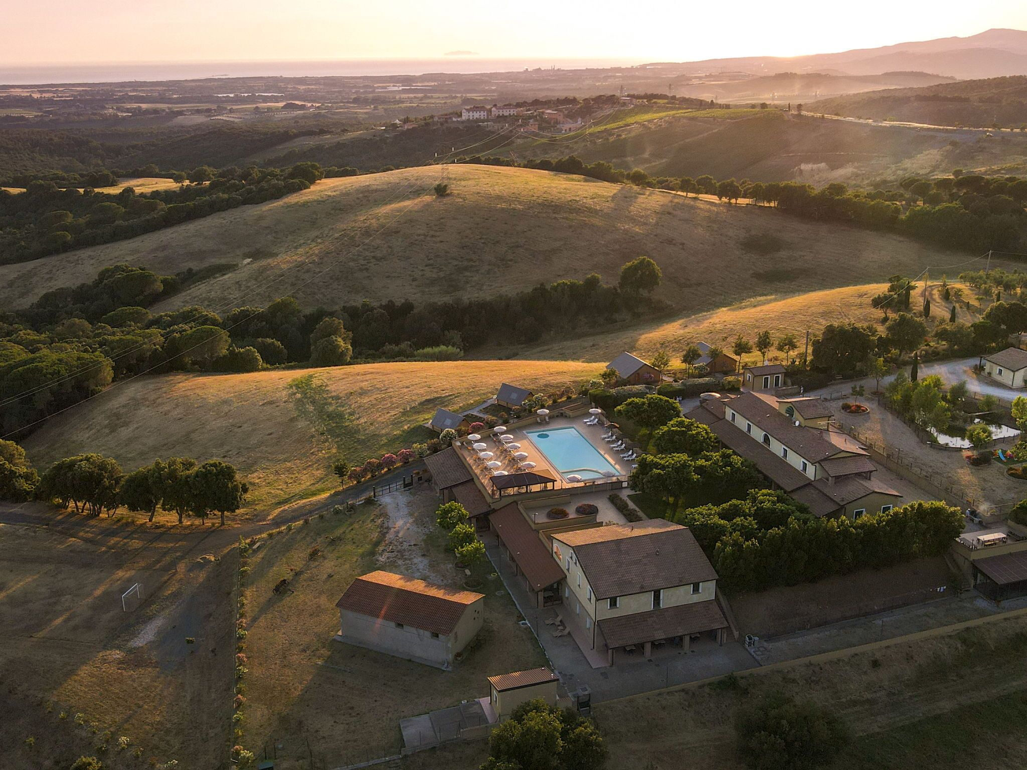 Vista aérea de um imóvel com piscina, vários edifícios e terreno montanhoso ao redor.