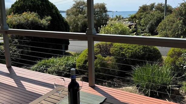 Uma área externa coberta com deck de madeira, uma garrafa de vinho e um copo sobre um tapete.