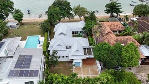 Un quartier résidentiel avec une maison dotée d’une piscine, de panneaux solaires et offrant une vue sur la plage et les bateaux.