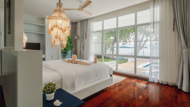 Une chambre avec un grand lit, un ventilateur de plafond, un lustre et une vue sur une piscine.