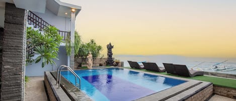 A swimming pool with a view of the sea, a stone structure, and lounge chairs.