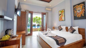 A hotel room with a bed, a TV, a desk with a kettle, and a view of the pool. - Barton Beach Inn (Penida Island)
