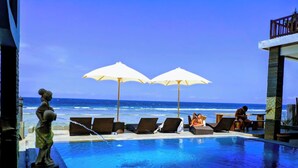 A poolside area with lounge chairs and umbrellas overlooking the ocean. - Barton Beach Inn (Penida Island)