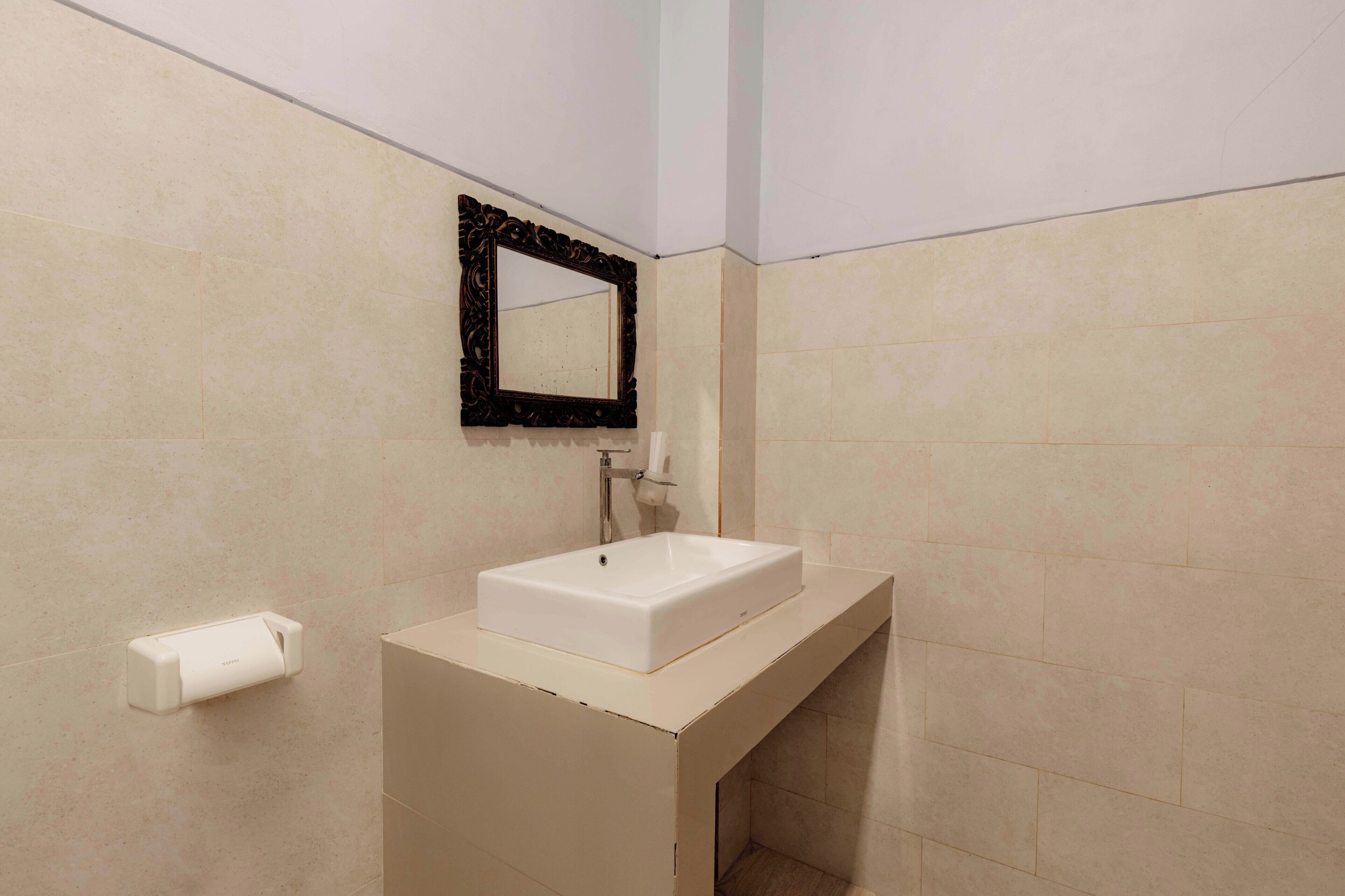 Une salle de bain avec un lavabo blanc, un miroir à cadre noir et un porte-rouleau de papier toilette fixé au mur.